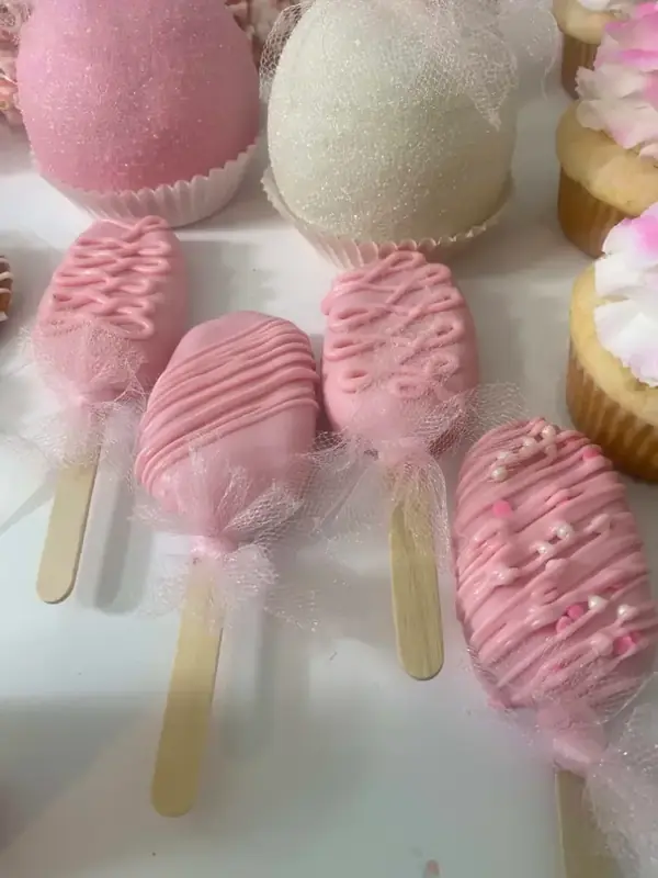 Pink drizzled cakesicles and sparkly cake pops on a dessert table, a sweet fit for a baby shower